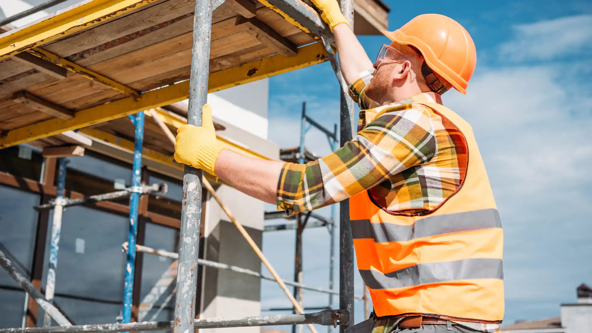 Zwei Kollegen mit Schutzhelmen und -westen stehen auf einer Baustelle, während im Hintergrund ein weiterer Mann zeigt.